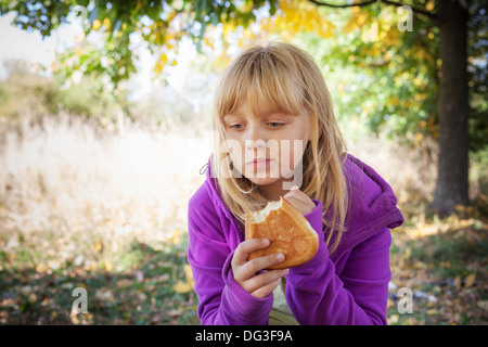 Little blond girl on a picnic in autumn park eats small pies Stock Photo