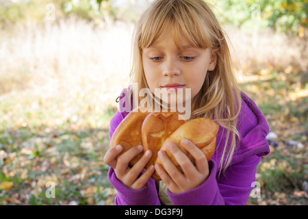 Little blond girl on a picnic in autumn park with small pies Stock Photo