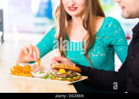 Friends or couple eating fast food with burger and fries in American fast food diner Stock Photo