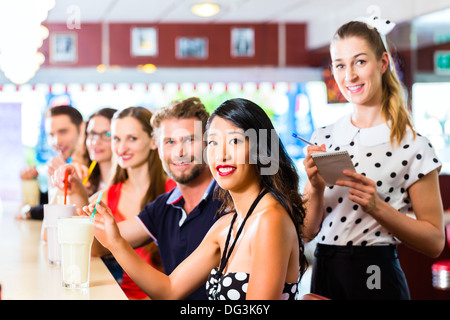 Friends or couples eating fast food and drinking milk shakes on bar in American fast food diner, the waitress is taking orders Stock Photo