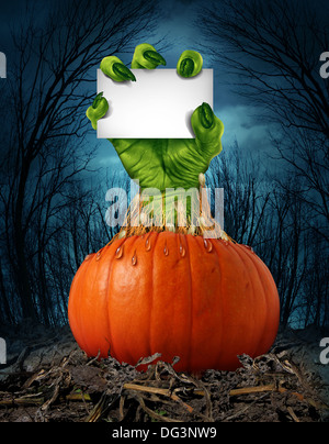 Zombie pumpkin sign with a green hand holding a blank sign card as a creepy halloween or scary symbol with textured skin wrinkled monster fingers coming out of a wet open pumpkin in a dark spooky forest. Stock Photo