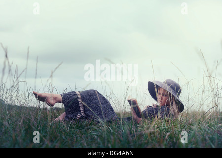 a woman in a romantic dress is lying on a meadow, reading a book Stock Photo