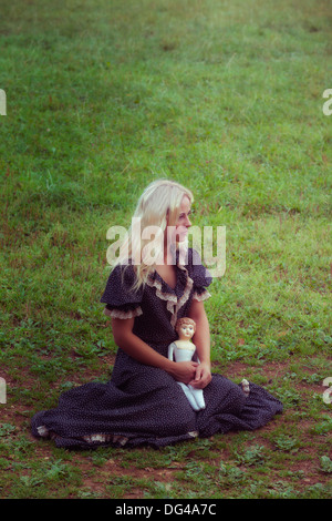 a woman in a romantic dress with an old doll on a meadow Stock Photo