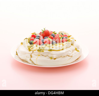 Pavlova made with fresh strawberries, raspberries, blueberries and passion fruit sitting in a meringue base on a pink background Stock Photo