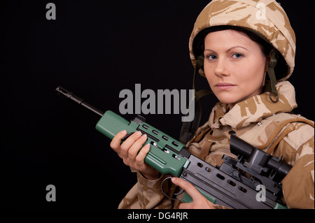 Female soldier holding an SA80 rifle, against a black background. She is wearing British Military desert camouflage uniform. Stock Photo