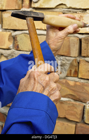 Elderly hand holding a hammer and chisel. Construction background. Stock Photo