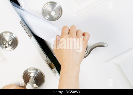 Angled horizontal photo of female hand cautiously taking paper notice from partially open front door of house Stock Photo