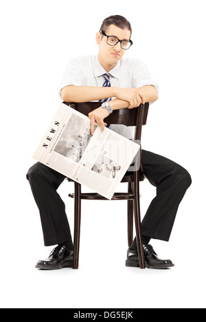 Disappointed young businessperson sitting on a wooden chair and holding a newspaper Stock Photo