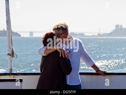 Middle-aged couple passionately kissing aboard a ferry boat on San Francisco Bay with the city and bridge in background. Stock Photo
