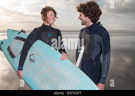 couple standing on beach with surfboards, one has a Gopro camera attached to surfboard Stock Photo