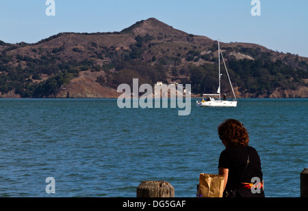 Woman sitting eating lunch at bay side in Sausalito, California with sailboat and Angel Island in the background Stock Photo