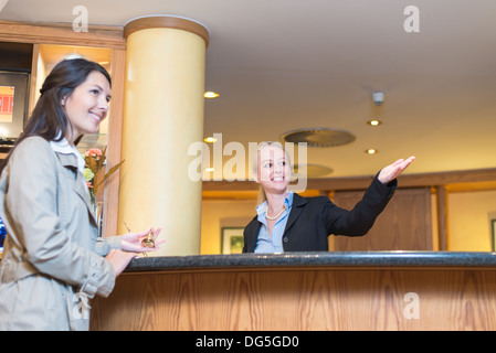 Low angle view of a beautiful friendly smiling receptionist behind the service desk in a hotel lobby helping a female guest Stock Photo