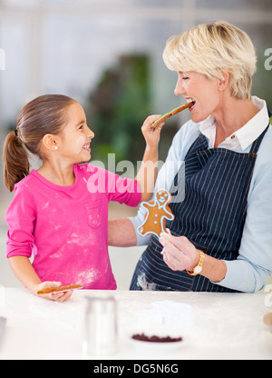 cute little girl feeding just baked gingerbread cookies to her grandmother Stock Photo
