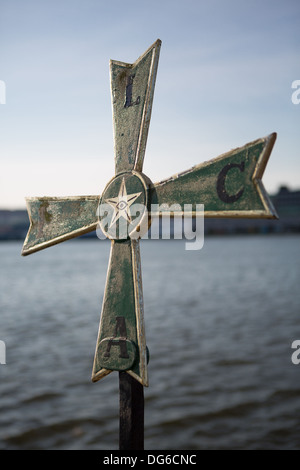 A metallic nordic cross photographed from a low angle against a blue sky with the harbor in the background Stock Photo