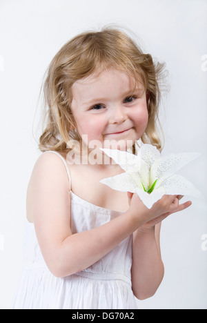 Beautiful innocent little girl dressed in white holding a large flower to her cheek, looking direct to camera, UK Stock Photo