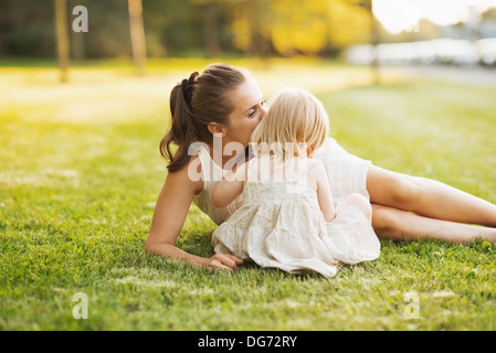 Mother kissing baby while sitting on meadow in park Stock Photo