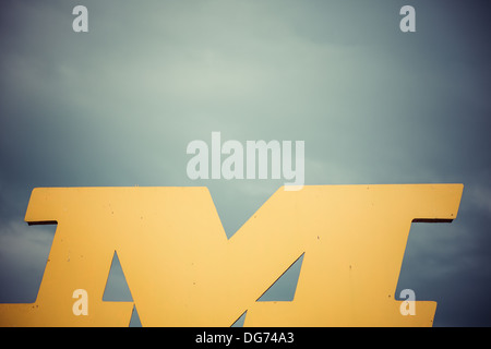 Yellow and designed shape of letter m with heavy sky in the background Stock Photo