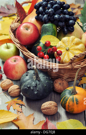 Fresh ripe pumpkins, apples, grape and nuts in wicker basket over wooden background Stock Photo