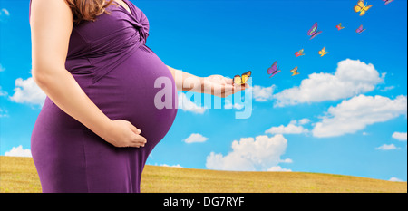 Pregnant woman holding her belly and butterflies on her hand, outside Stock Photo