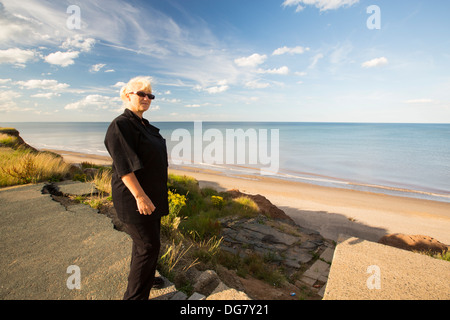 Sylvia Hughes stands next to the edge of collapsing coastal cliffs at Aldbrough on Yorkshires East Coast, UK. Stock Photo