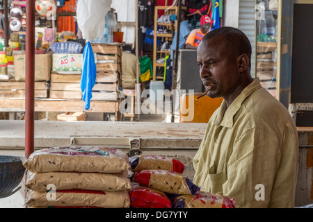 Senegal, Saint Louis. A Shopkeeper with a Chewing Stick in his Mouth, for Cleaning Teeth. Selling Bags of Rice. Stock Photo