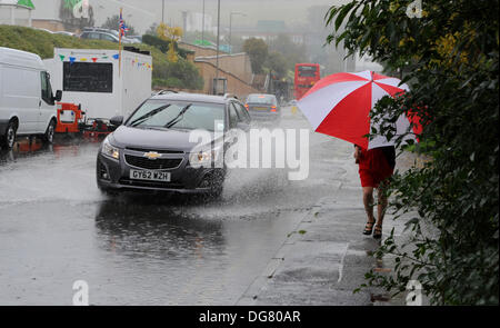 A woman with an umbrella runs past flood water on a Brighton road as heavy rain causes problems in Sussex today Stock Photo