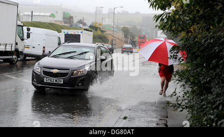 A woman with an umbrella runs past flood water on a Brighton road as heavy rain causes problems in Sussex today Stock Photo