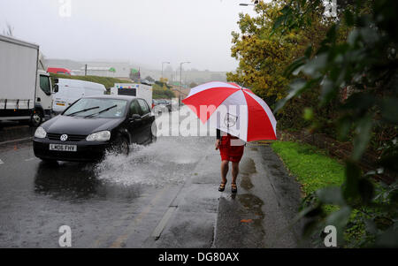 A woman with an umbrella runs past flood water on a Brighton road as heavy rain causes problems in Sussex today Stock Photo