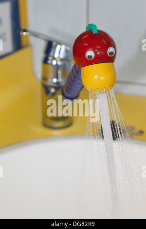 Tap in a red and yellow novelty fun duck's head design switched on spraying water into a wash basin in a children's washroom Stock Photo