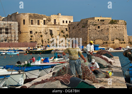 Fishermen mending nets in boat harbor outside medieval city wall, Gallipoli, Puglia, Italy Stock Photo