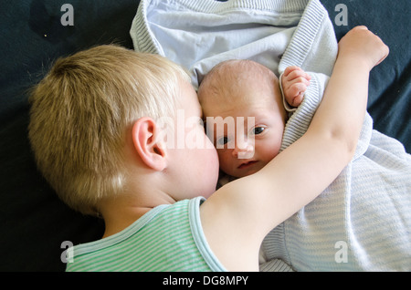 Baby with big eyes beeing cuddled by his older brother Stock Photo