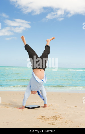 young businessman doing handstand on the beach after a big deal Stock Photo