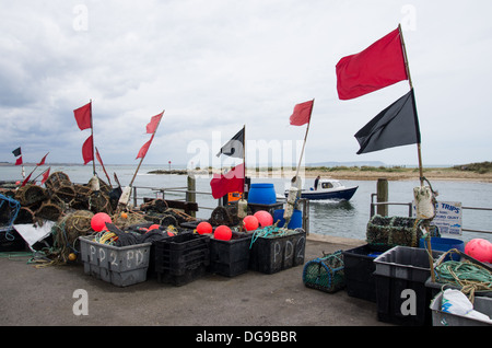 A scene in a fishing village of Mudeford with fishing tools and red flags on a sea shore and a boats passing by on an overcast day.