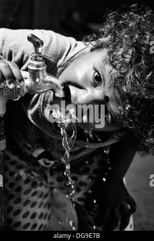 Young Indian girl / infant drinking water from a tap in a rural Indian village. Andhra Pradesh, India. Black and White Stock Photo