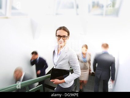 Portrait of smart businesswoman looking at camera on background of other people ascending and descending staircase Stock Photo