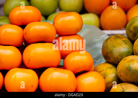 A pile of fresh persimmon fruit is displayed on a produce stand on a local street market stall in Siem Reap, Cambodia Stock Photo