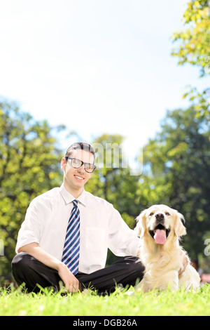 Young smiling man sitting on a green grass next to his dog in a park Stock Photo