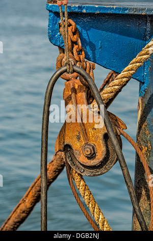 A closer view of a trawler fishing boat's showing a rusted pulley, chain and ropes. Stock Photo