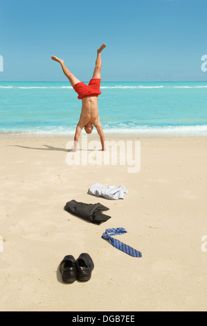 young businessman doing handstand on the beach after a big deal Stock Photo