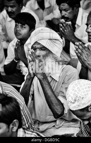 Old Indian man in prayer whilst waiting at Sri Sathya Sai Baba mobile outreach hospital. Andhra Pradesh, India. Monochrome Stock Photo