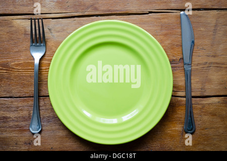 green empty dish on the vintage wooden table with fork and knife
