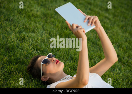 Mid adult women lying in park using digital tablet