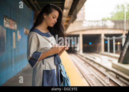 Mid adult women using mobile phone on subway platform, Brooklyn, New York Stock Photo