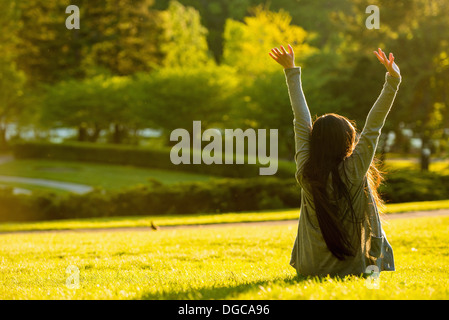 Young female sitting with arms raised in park Stock Photo