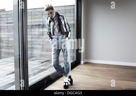 Young woman leaning against window, looking down Stock Photo