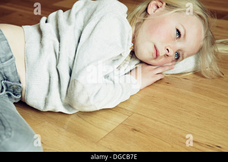 Young girl lying on wooden floor, looking away Stock Photo