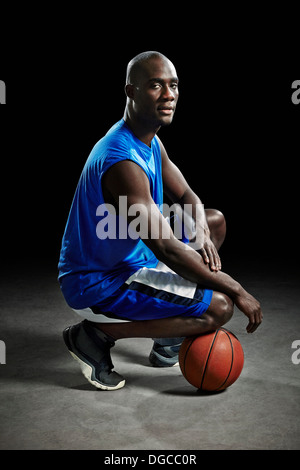 Studio portrait of basketball player kneeling on ball Stock Photo