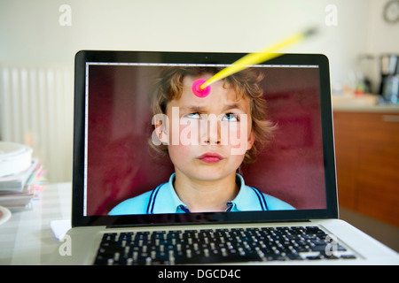 Boy looking up from laptop screen at toy arrow Stock Photo