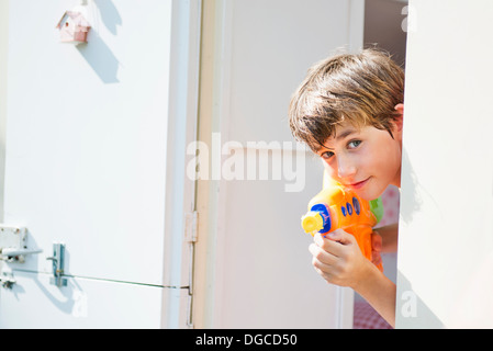 Boy holding water pistol and peering out of caravan, portrait Stock Photo