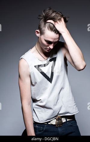 Young man with hand in hair looking down, studio shot Stock Photo